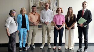 Auf diesem Foto sind sieben Personen zu sehen, die vor einer Wand stehen.