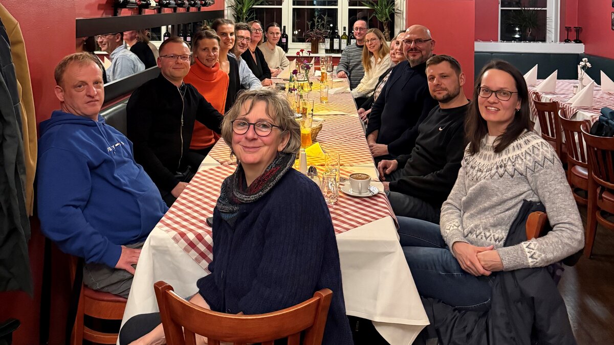 Auf diesem Foto sind 15 Menschen zu sehen, die an einem Tisch sitzen