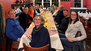 Auf diesem Foto sind 15 Menschen zu sehen, die an einem Tisch sitzen
